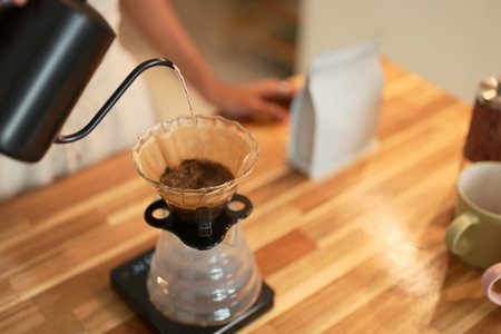 Close up of hand pouring hot water into pour over coffee dripper on a wooden kitchen counter.の写真素材