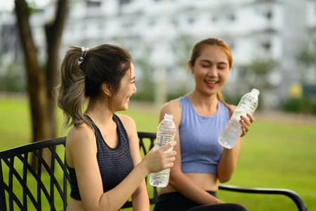 Two cheerful female friends cooling down with bottled water after a workout.の写真素材
