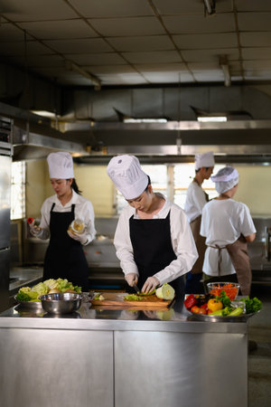 Chef apprentice working on vegetable preparation in a busy kitchen..の写真素材