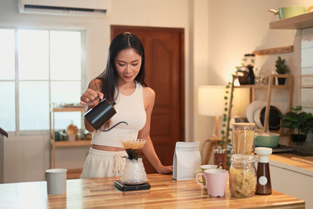 Young woman pouring hot water into pour over coffee dripper on a wooden kitchen counter.の写真素材