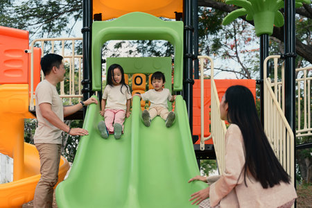 Parents watching and guiding their children as they play on a slide at the playground.の写真素材