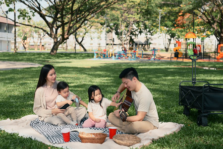 Parents and two children sharing a joyful outdoor meal during a weekend picnic in a green park.の写真素材