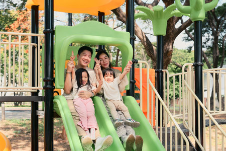 Happy family of four sliding together at a playground.の写真素材