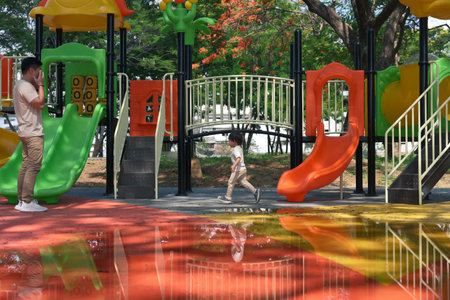 Father watching his little child explore and play at a colorful playground on a sunny day.の写真素材