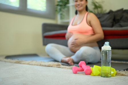 Pregnant woman sitting on the floor with a bottle of water and two dumbbells in front of her.の写真素材