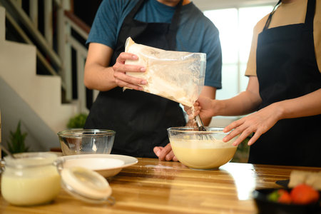 Young couple preparing pancake ingredients together in cozy kitchen.