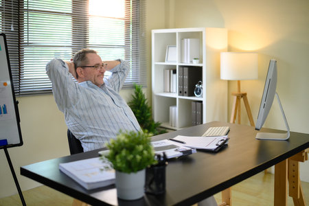 Senior man relaxing after completing tasks in a modern workspace.の写真素材
