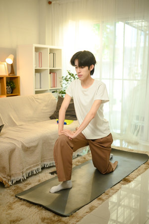 Smiling young asian man practices yoga on a mat in his living room.の写真素材
