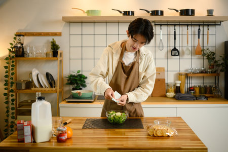 Young man pours dressing onto a bowl of fresh vegetable salad.の写真素材