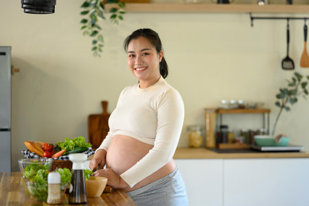 Happy pregnant woman stands at kitchen counter, preparing a wholesome meal.の写真素材