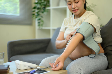Pregnant woman checks her blood pressure at home. Maternal wellness and health care concept.の写真素材