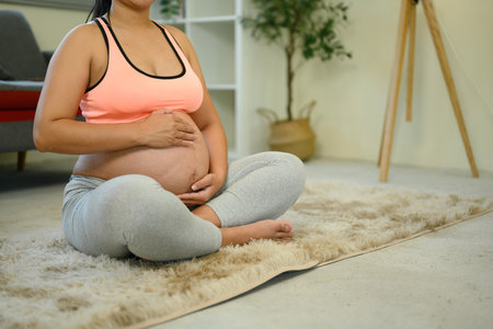 Pregnant woman in activewear sits on the floor with hands resting on her bump.の写真素材
