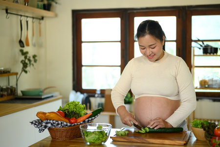 Happy pregnant woman stands at kitchen counter, preparing a wholesome meal.の写真素材