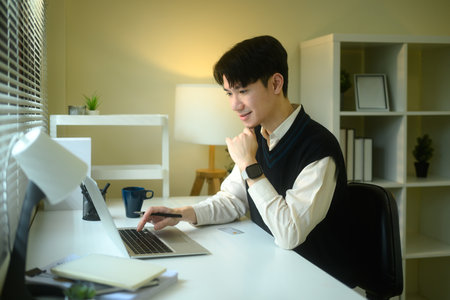 Young entrepreneur in a sweater vest uses a laptop at a minimalist desk.の写真素材