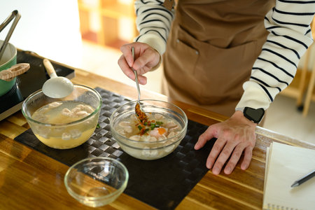 Hands seen seasoning a clear broth soup with meatballs and herbs.の写真素材