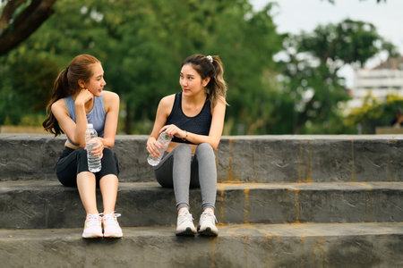 Sporty women take a break on concrete steps with water bottles in hand.の写真素材