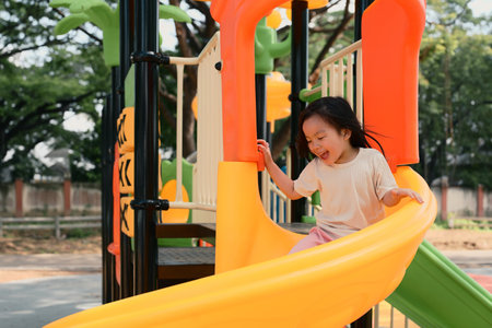 Cheerful little girl sliding at colorful playground.の写真素材