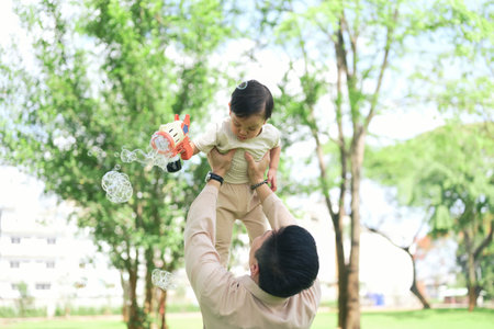 joyful dad lifts his toddler high in the air as the child holds a bubble gun.の写真素材