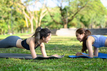 Happy female friends doing plank exercises on yoga mats in the park.の写真素材