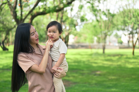 Asian mother and her toddler stroll through a lush green park.の写真素材