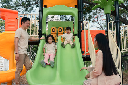 Smiling siblings enjoy a fun ride down a double slide as their parents stand by.の写真素材