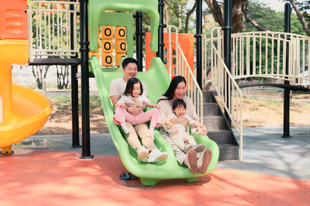 Parents and children enjoy a fun moment riding down a double slide, laughing during a sunny day.の写真素材