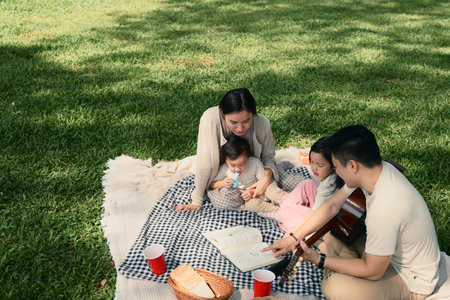 Parents read a book to their young children while relaxing on a blanket outdoors.の写真素材