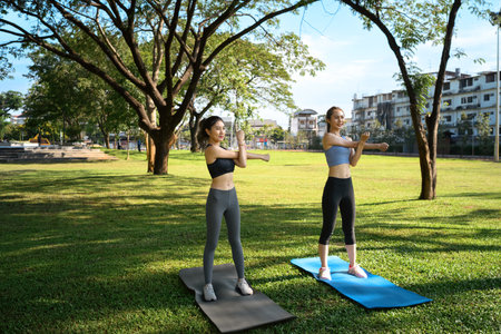 Two young women stretching outdoors on yoga mats in a city park.の写真素材