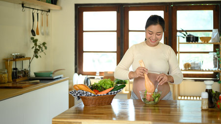 Happy pregnant woman prepares a healthy salad at home.の写真素材