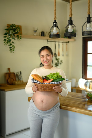 Pregnant woman preparing a nutritious meal with fresh ingredients in home kitchen.の写真素材