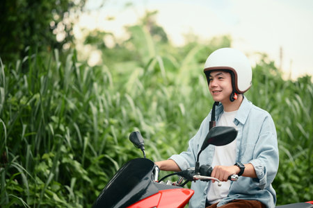 Smiling young man wearing helmet riding a motorcycle on a quiet residential street.の写真素材
