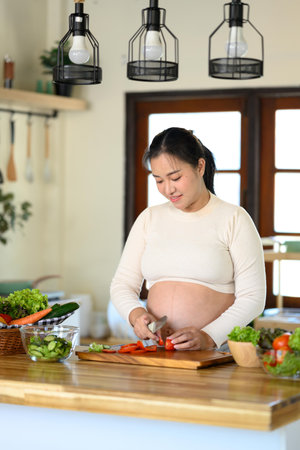 Happy pregnant woman preparing a nutritious meal with fresh ingredients in home kitchen.の写真素材