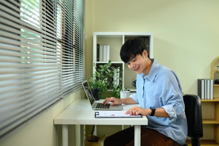 Happy male entrepreneur analyzing business charts and using laptop at desk.