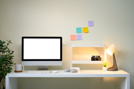 Modern workspace with desktop monitor, sticky notes on wall, desk lamp, and creative decor.の写真素材