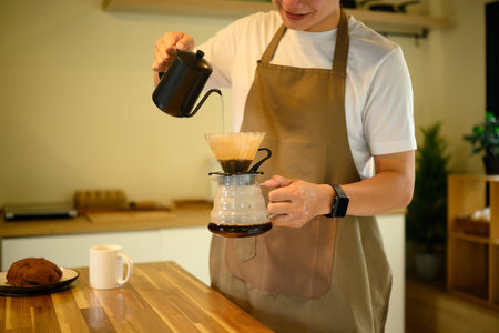 Man wearing an apron preparing pour over coffee in a cozy kitchen.の写真素材