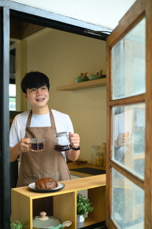 Young man holding a fresh cup of coffee and carafe, smiling.の写真素材