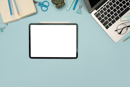 Flat lay of digital tablet with blank screen surrounded by office supplies and laptop.の写真素材