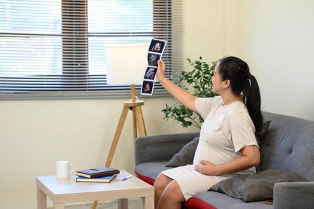 Happy pregnant woman admiring sonogram photos and gently touching her belly.の写真素材