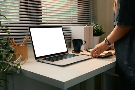 Stylish workstation with a blank laptop screen and woman writing on a notebook.の写真素材