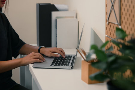 Side view of young woman working on a laptop in a tidy home office.の写真素材
