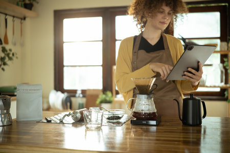 Young woman uses digital tablet while preparing pour over coffee in a stylish kitchen.の写真素材