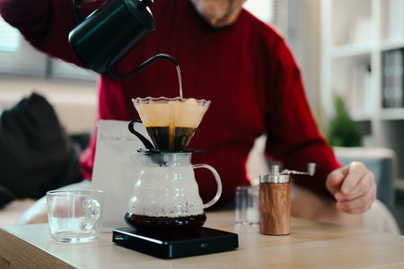 Senior man in a red sweater making pour over coffee with a glass dripper and kettle.の写真素材