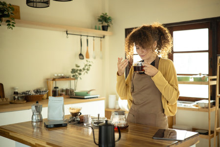 Young woman enjoys the aroma of a fresh cup of coffee in a warm kitchen.の写真素材