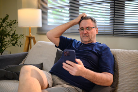 Older man sitting on a couch looking at a smartphone.の写真素材