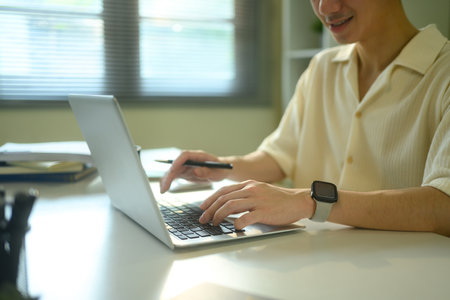 Cropped image of man typing on a laptop keyboard at a bright white desk.の写真素材