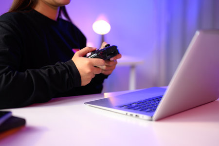 Close up of gamer holding a console controller while playing on a laptop.の写真素材