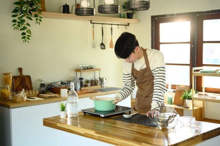 Smiling man in an apron preparing meal in a sunlit modern kitchen.の写真素材