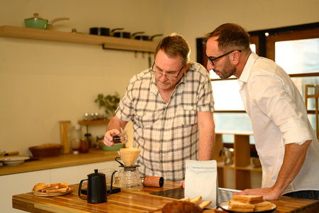 Mature father and adult son preparing fresh pour-over coffee in a cozy kitchen.の写真素材