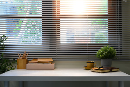 Stylish home office desk by the window with sunlight streaming through blinds.の写真素材