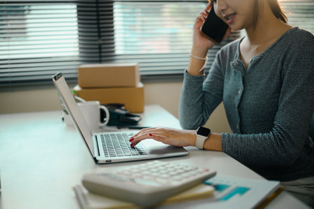 Young woman business owner communicating with client and checking inventory on laptop.の写真素材